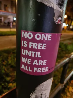 A sticker with a powerful message about freedom and equality.  The sticker is affixed to a dark pole, suggesting it may be part of a street art or activist campaign.
