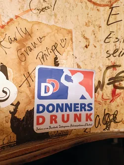 A sticker with a logo and text. The logo is a baseball-style graphic with the letters 'DD' and an illustration of a person drinking. The text reads 'DONNERS DRUNK' and includes instructions to follow on Facebook and Instagram.