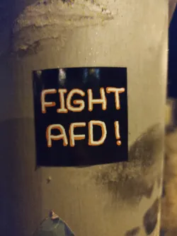 A black sticker with orange text saying "FIGHT AFD!" is affixed to a pole.