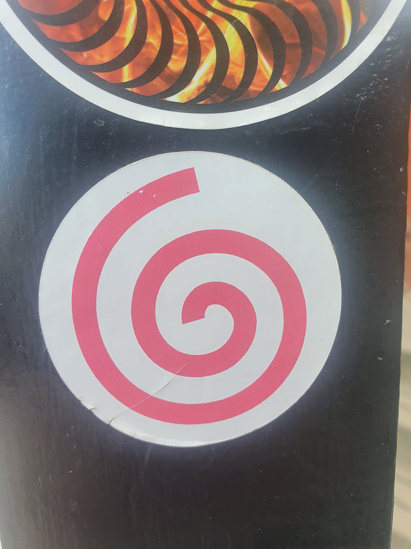A round sticker with a pink spiral on a white background. The sticker is slightly damaged.