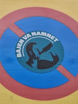 A sticker featuring a silhouette of a man drinking from a bottle, set within concentric circles of red, blue and yellow. The text 'Bajen va namnet' is visible around the central image.