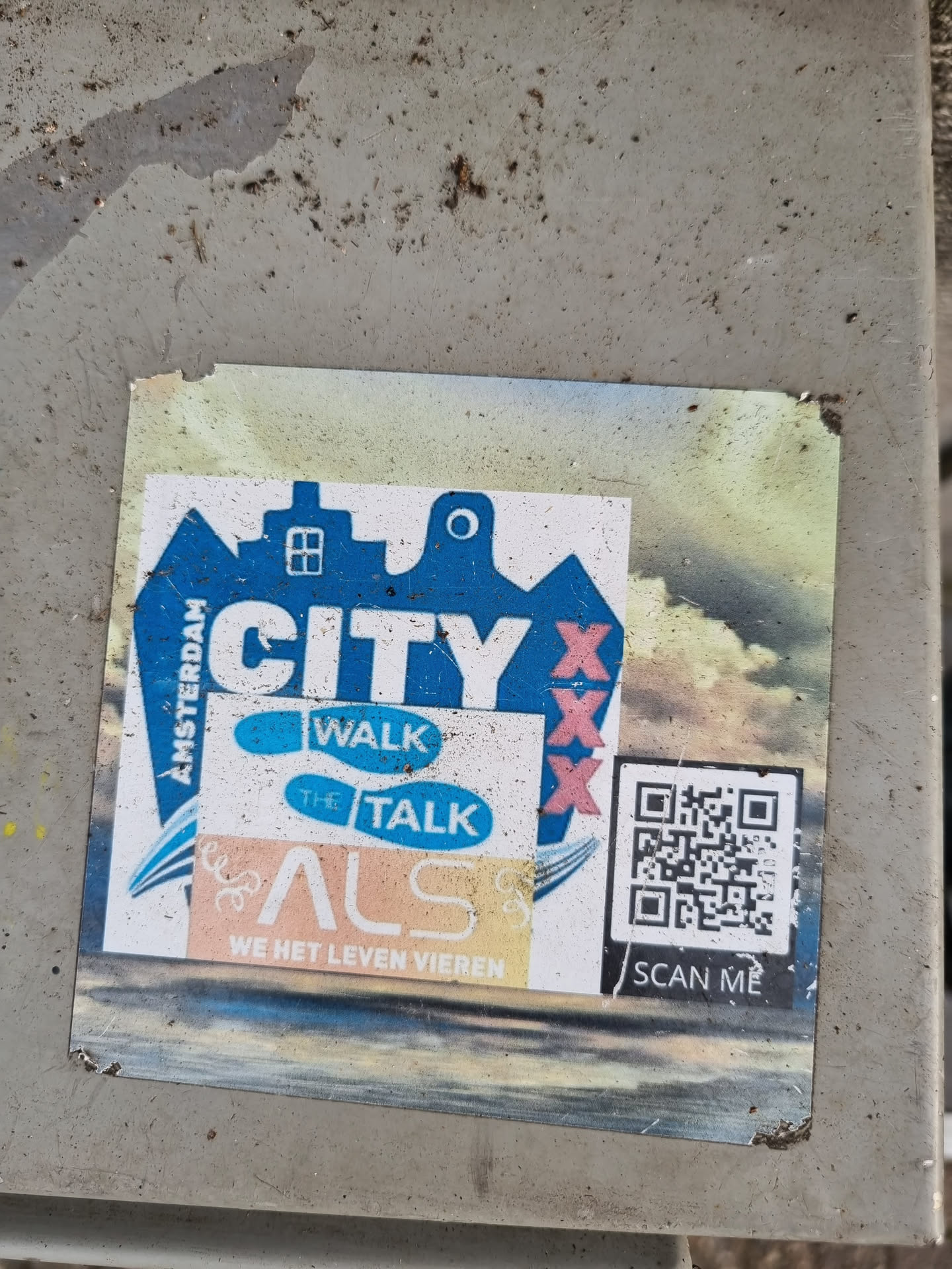 A sticker featuring a city logo with the text 'CITY' and 'XXX', along with the words 'WALK', 'TALK', 'ALS', and 'WE HET LEVEN VIEREN'. A QR code is also present, with the instruction 'SCAN ME'.