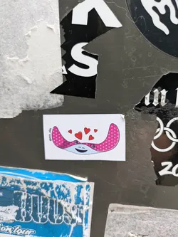 A cute sticker featuring a pink stingray with white polka dots and several red hearts floating above it. The stingray has a smiling face.