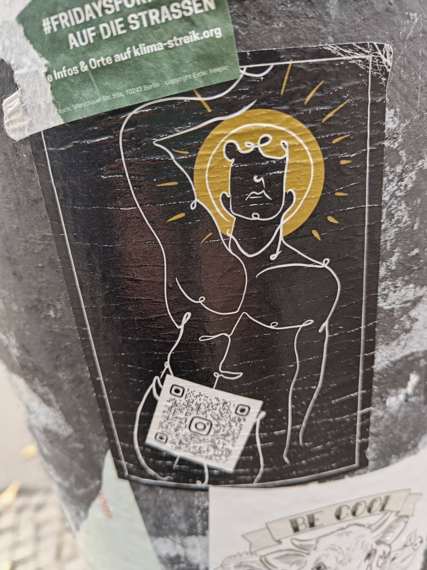 A dark-colored sticker features a minimalist line drawing of a muscular male figure, reminiscent of a classical statue.  The figure is backlit by a stylized sunburst. A QR code is located near the bottom of the sticker.
