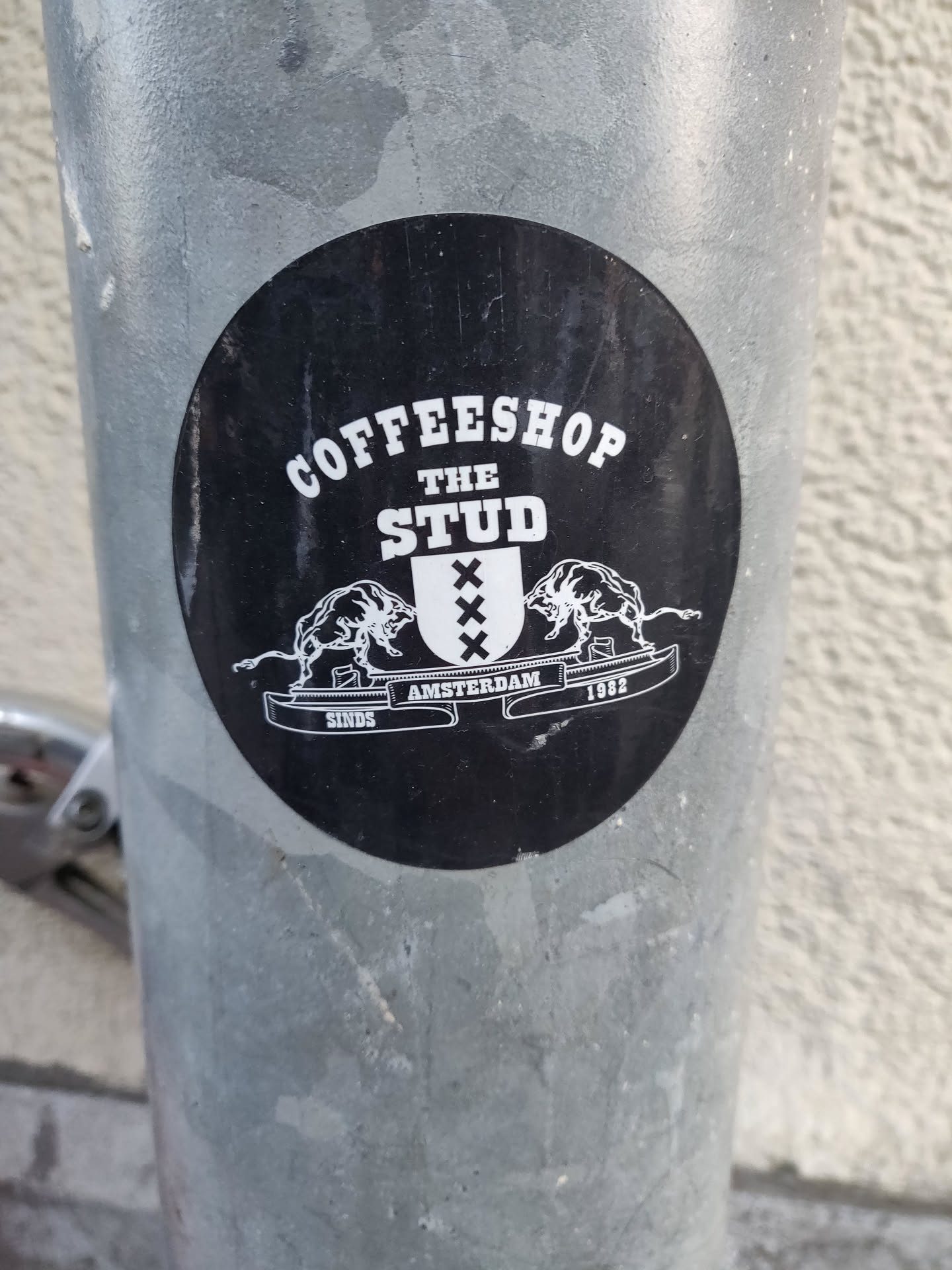 A black and white sticker for Coffeeshop The Stud in Amsterdam. It features a coat of arms with two bulls and the text "XXX Amsterdam 1993 SINCE".