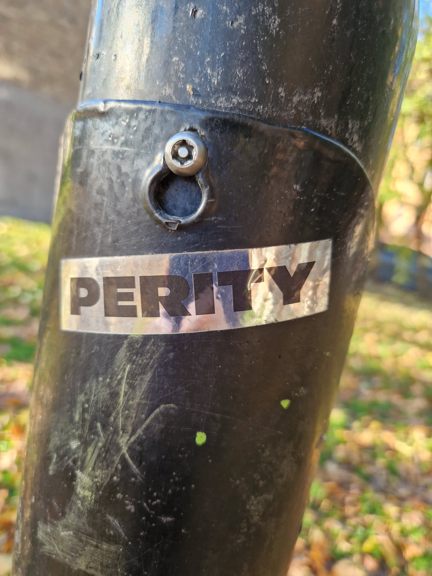 A silver Perity sticker affixed to a dark-colored metal pole outdoors. The sticker is rectangular and features the word "PERITY" in bold, uppercase lettering. The background of the sticker appears slightly reflective.