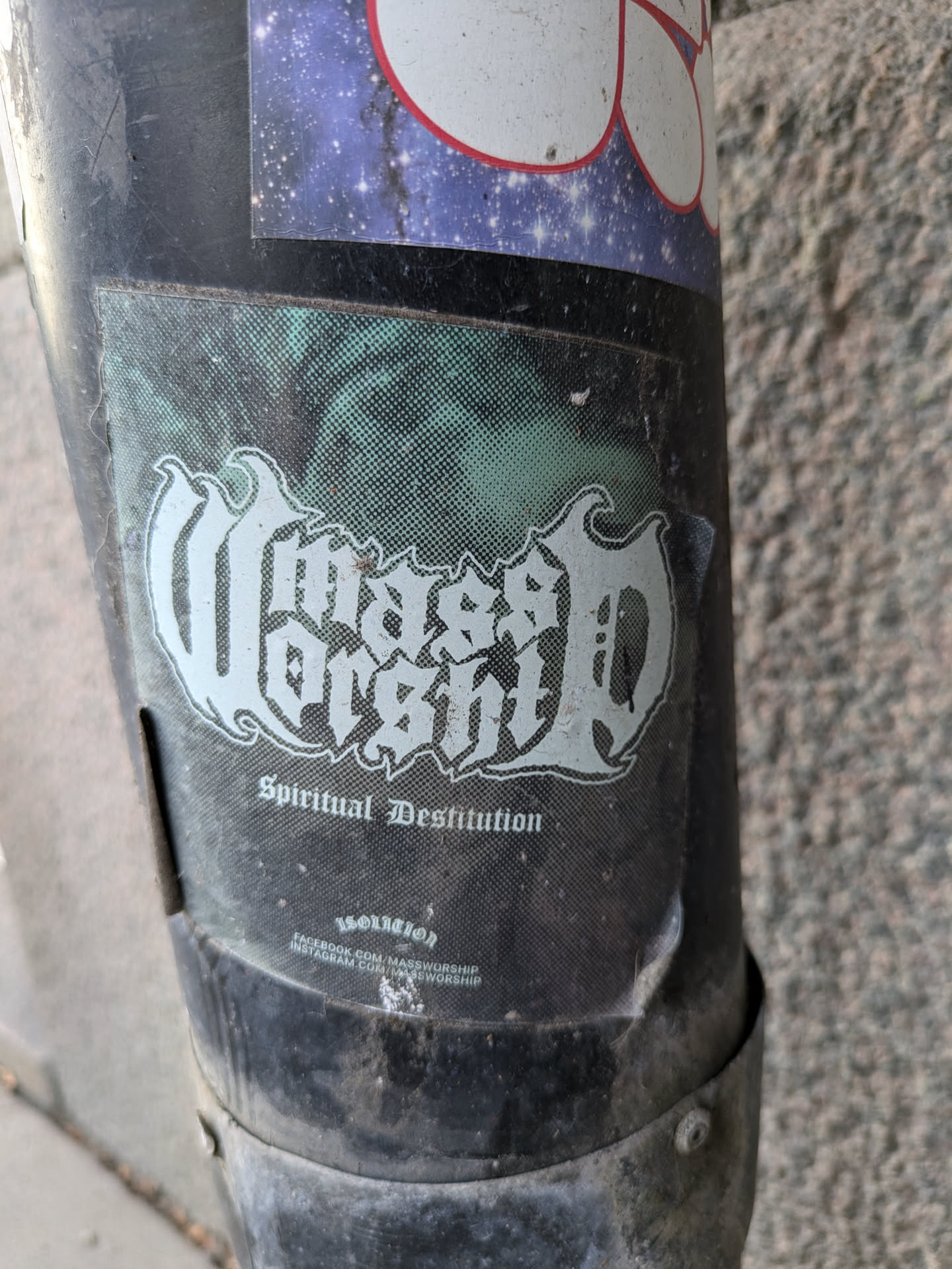 A sticker featuring the band Mass Worship and their album "Spiritual Destitution". The sticker is placed on a dark cylindrical object. The sticker has a worn look.