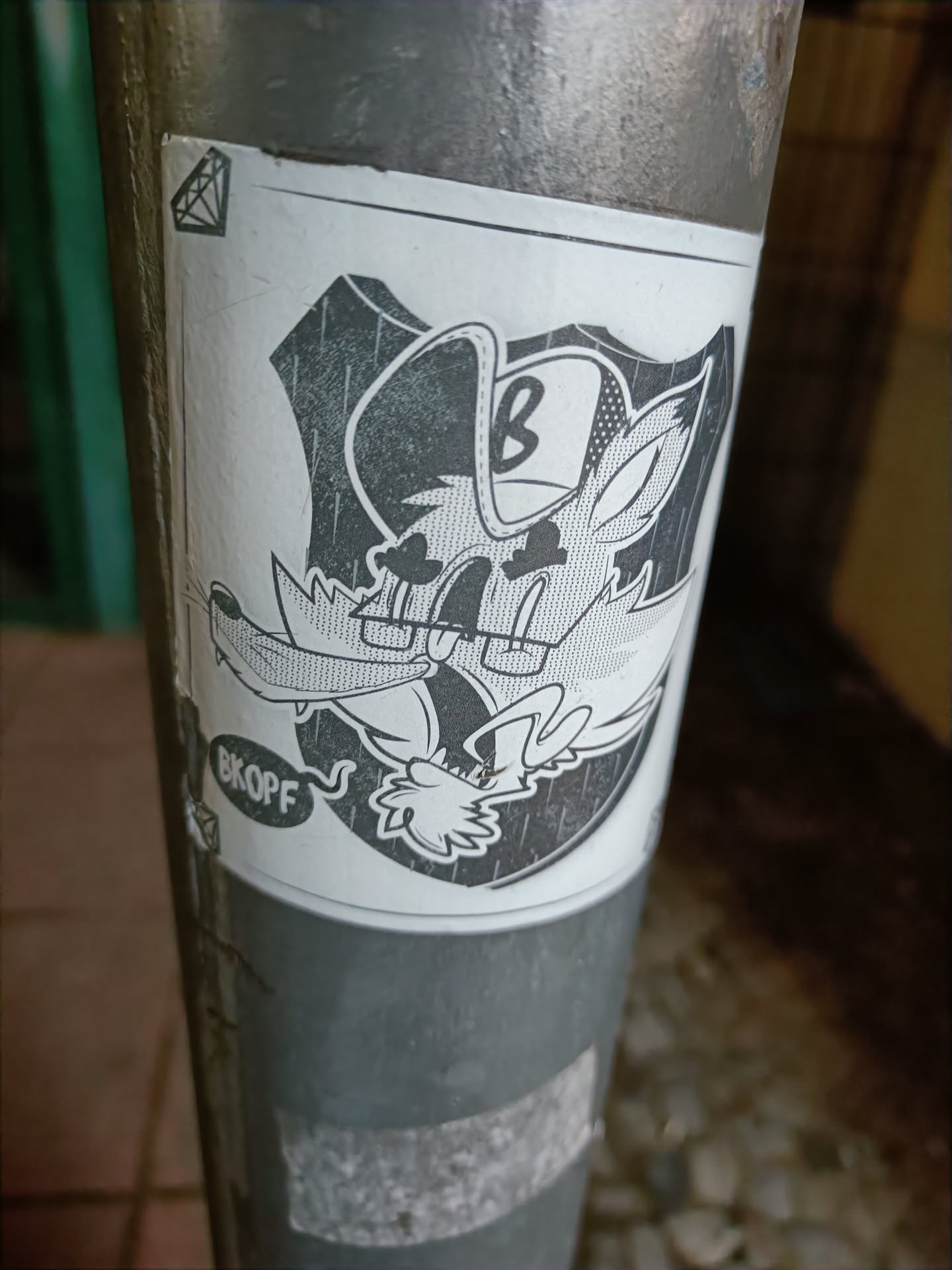 A grayscale sticker featuring a cartoon fox wearing a baseball cap with the letter 'B' on it. The fox is depicted in a shield-like shape and has a speech bubble that says 'BKOFF'. The sticker has a slightly worn look.
