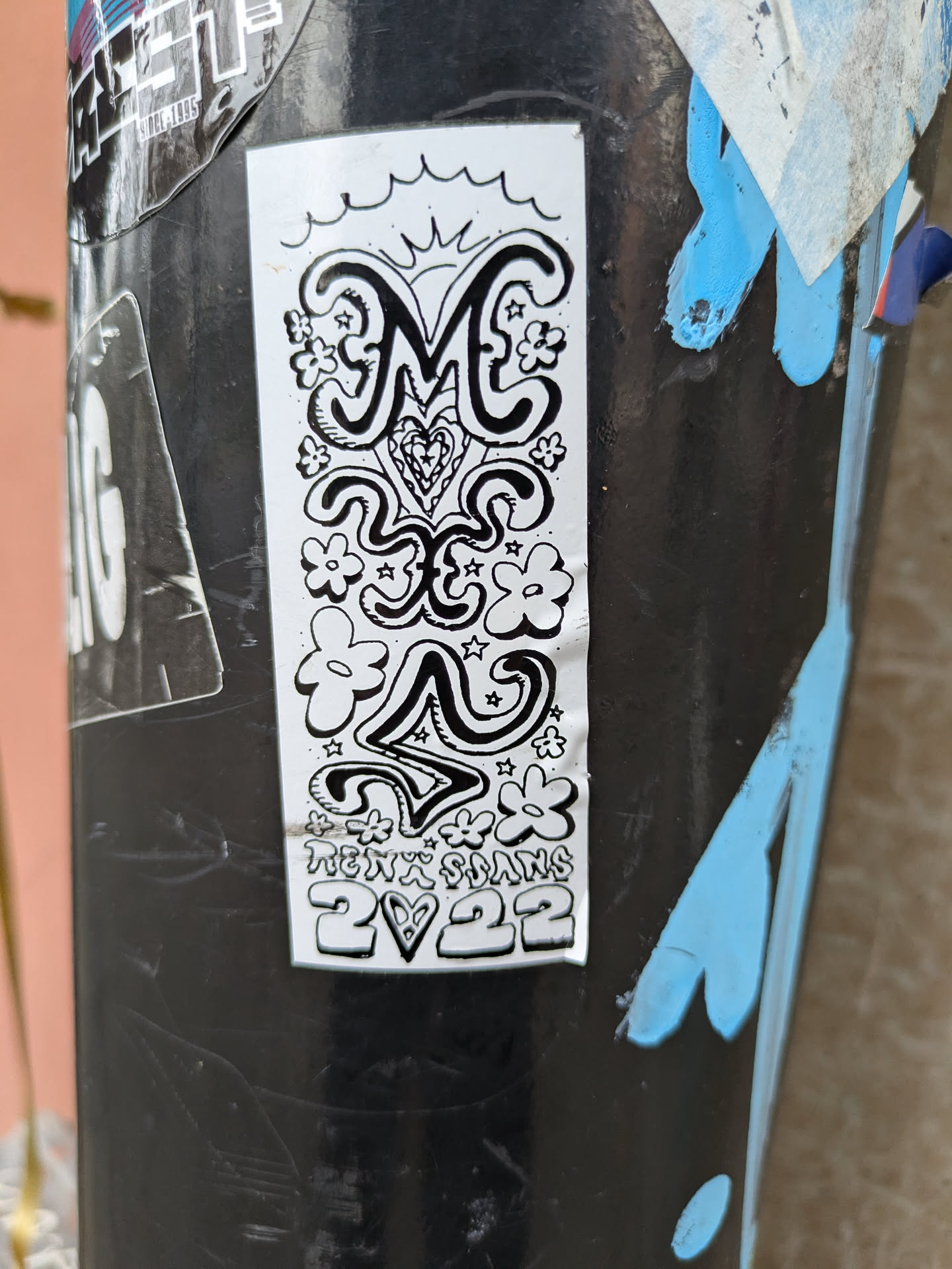A black and white sticker featuring stylized lettering of 'ME', surrounded by flowers, stars, and a heart. The text 'Hexx Sams 2♡22' is present at the bottom. The style is reminiscent of 70s psychedelic art.