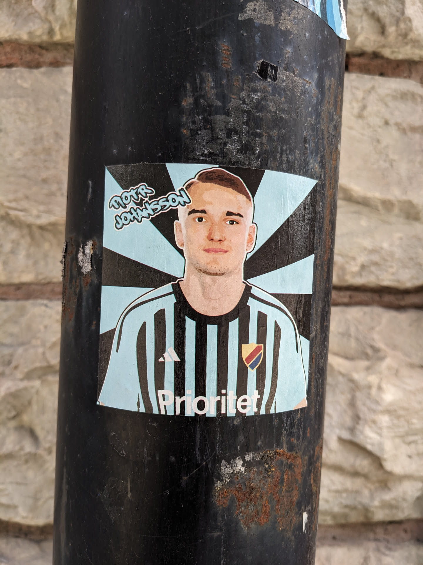 A sticker featuring a portrait of Piotr Johansson, possibly a football player, in a light blue and black striped jersey with the word 'Prioritet' visible.  The sticker has a retro comic book style design.