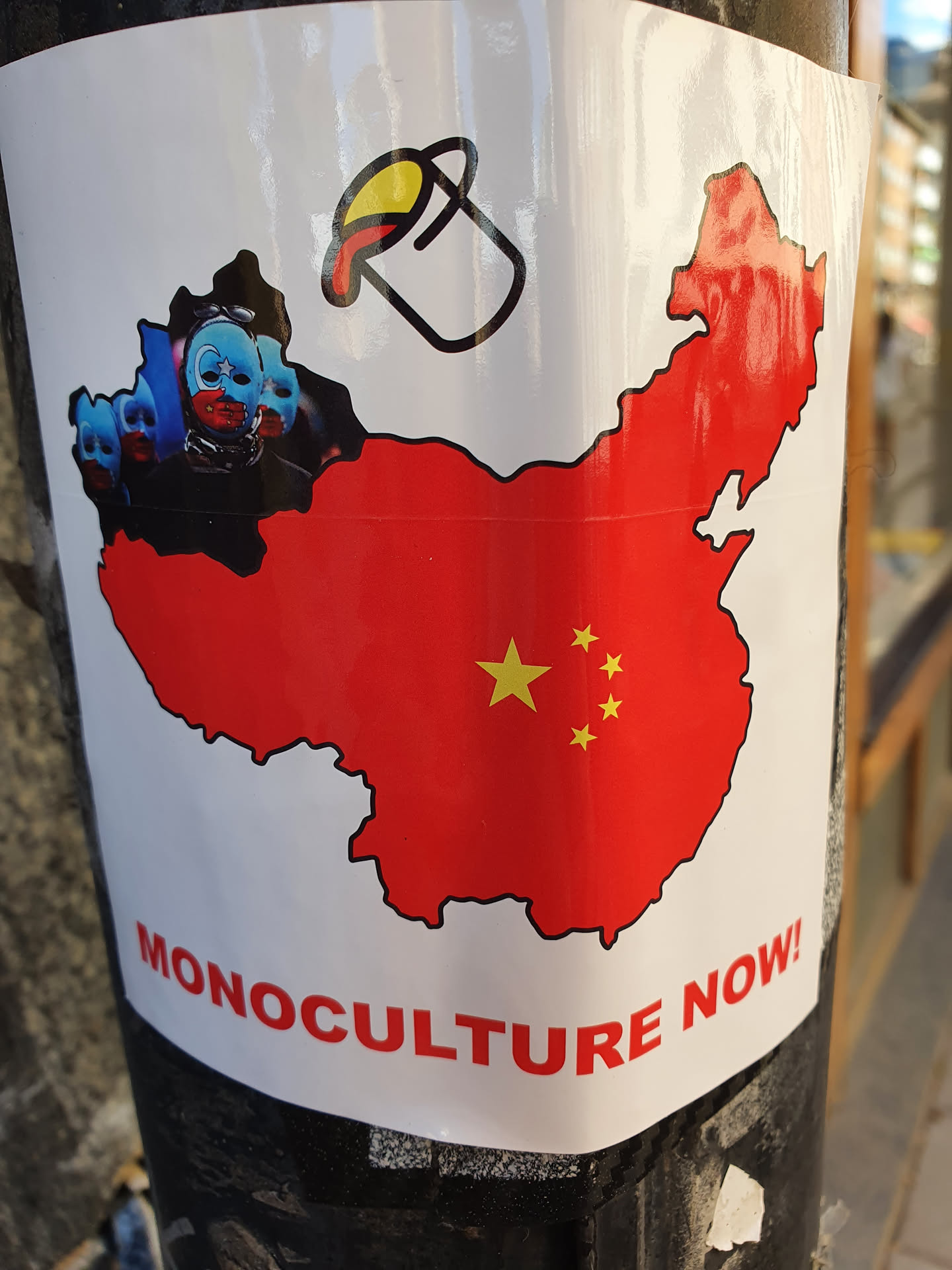 A sticker depicting a map of China being painted red with a bucket of paint, and a line of masked figures. The text 'Monoculture Now!' is at the bottom.