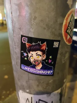 A sticker featuring an anime-style illustration of LukesGaming97 with cat ears.  The sticker has a dark background with pastel stars. The Twitch logo is also visible.