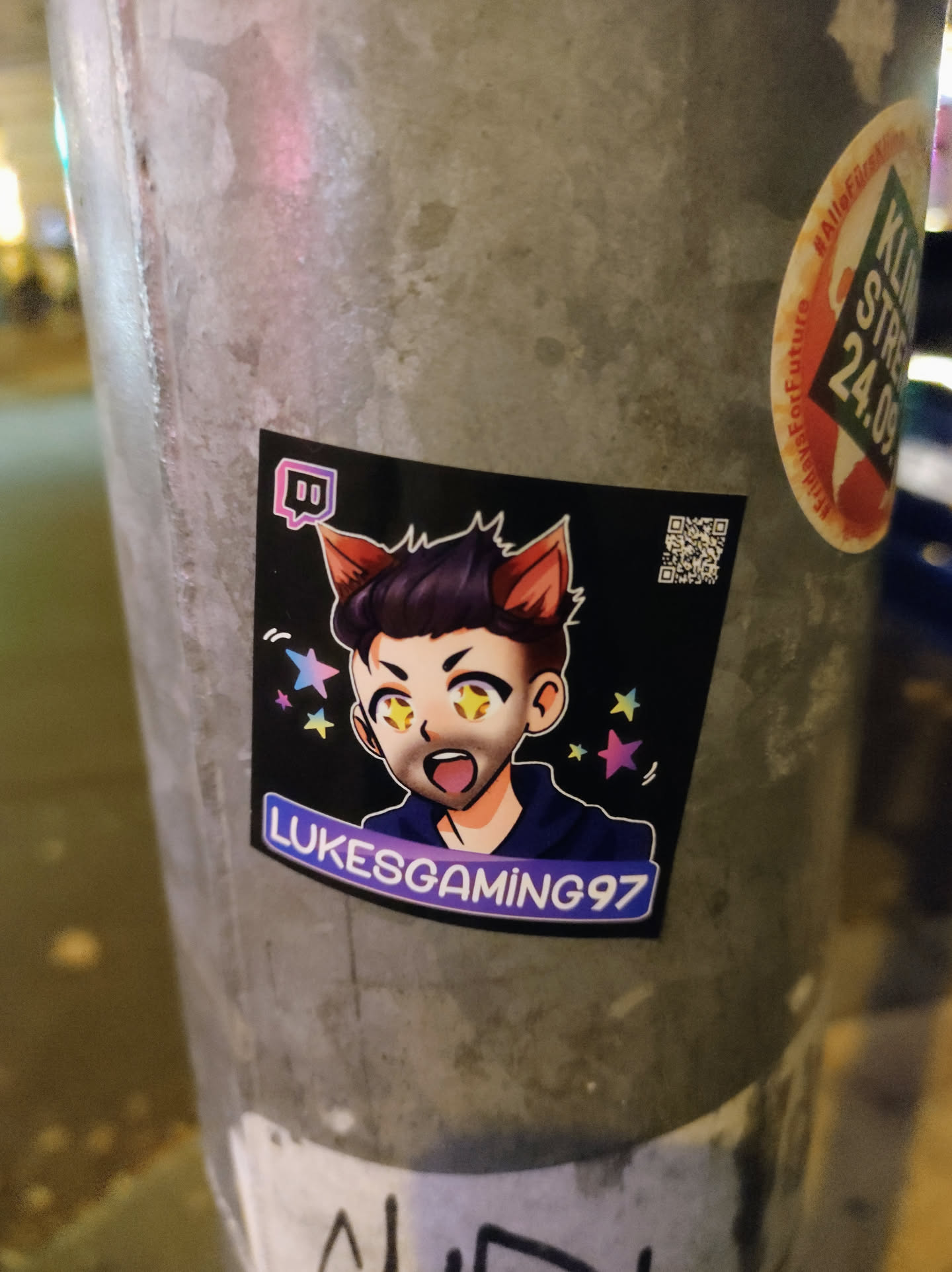 A sticker featuring an anime-style illustration of LukesGaming97 with cat ears.  The sticker has a dark background with pastel stars. The Twitch logo is also visible.