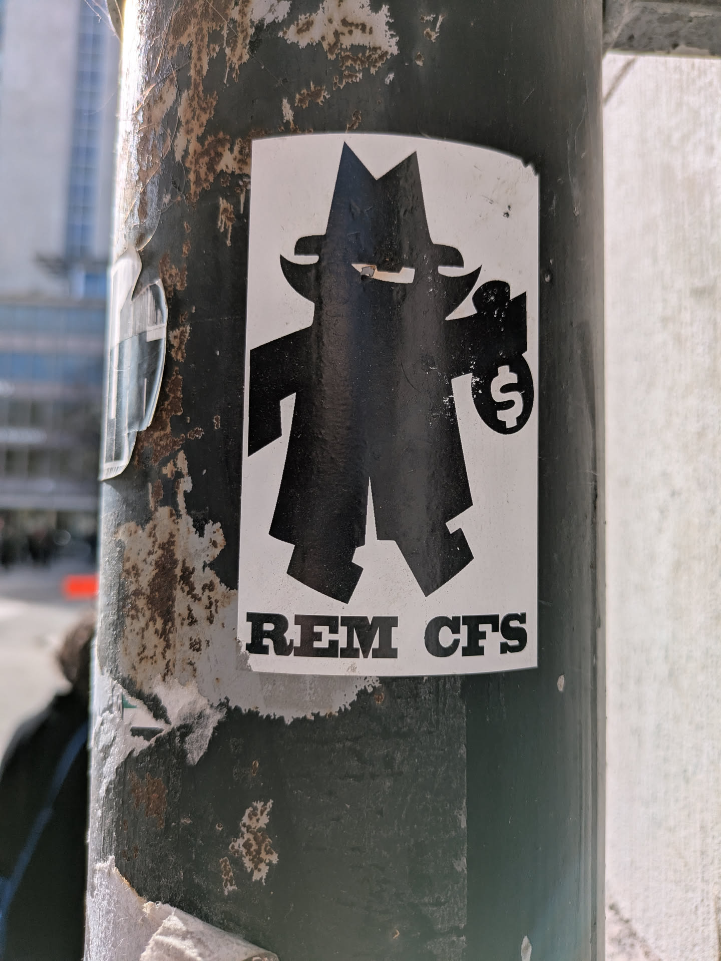 This sticker depicts a simplified, cartoon-like figure wearing a hat and coat, suggestive of a spy or a criminal. The figure holds a bag with a dollar sign on it. Below the figure, the text "REM CFS" is printed. The sticker is adhered to a pole.