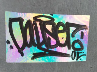 A holographic sticker with a vibrant iridescent background and black graffiti-style lettering. The main text appears to be 'Wiser', and there's a small '05' at the bottom right.  The sticker has a glossy, reflective surface.