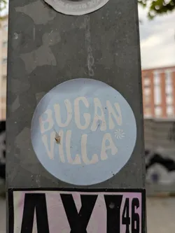 This is a round sticker with a light blue background. The text "Bogan Villa" is written in a retro-style, sans-serif font in white color. There's a small asterisk-like design between the words.