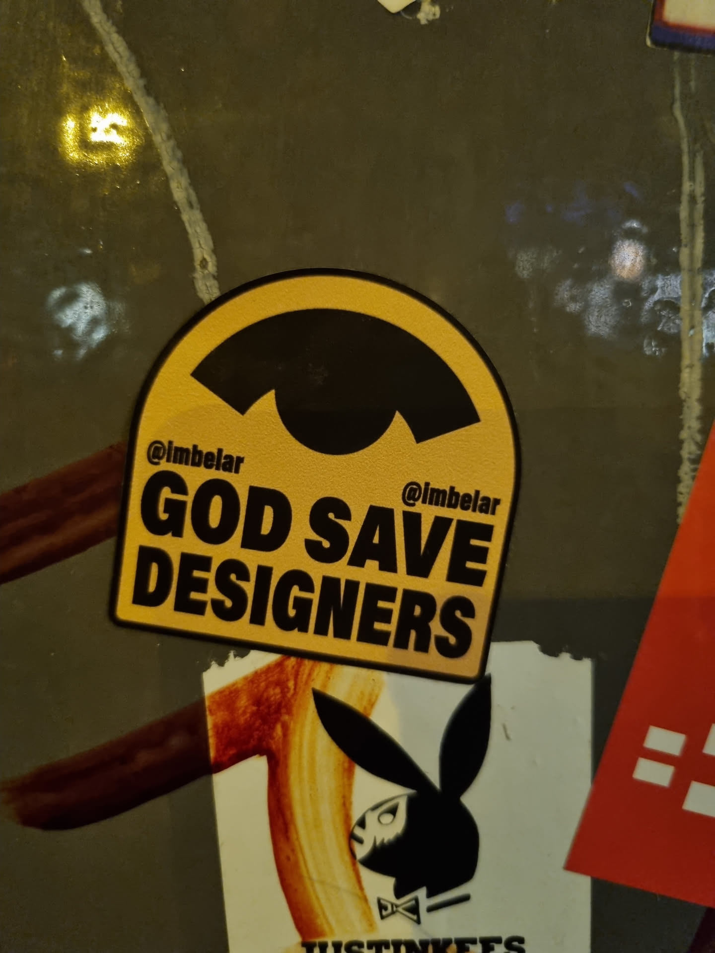 A yellow and black sticker with the text "GOD SAVE DESIGNERS" and the Instagram handle @imbelar. The sticker has a unique arched shape.