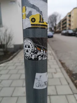 A rectangular sticker adhered to a metal pole, featuring a black and white design with accents of red and yellow. The left side displays a circular crest with '1912' at the top, 'BIF' in the center within a shamrock-like emblem, and 'BRYNÄS' below, all in white on a black background. The right side depicts a stylized crowd of diverse faces, rendered in black and white, with several red and yellow flags or banners waving above them. The overall aesthetic is graphic and illustrative, celebrating a sports club's history and supporters.