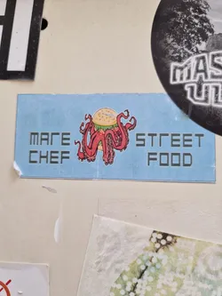 A sticker featuring an octopus holding a burger on a light blue background. The text 'Mad Chef' and 'Street Food' is displayed on the sticker.