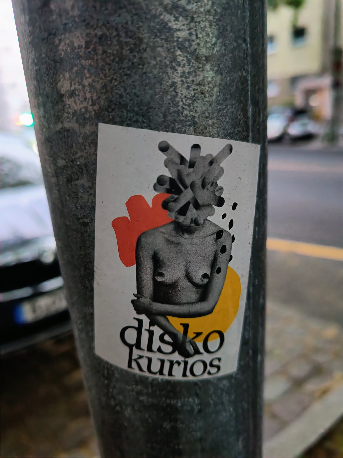 A sticker featuring a stylized female torso with an abstract headpiece. The text 'disko kurios' is visible at the bottom. The sticker has a colorful design with orange and yellow accents. 