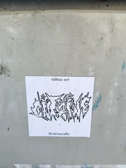 A sticker featuring a black line art design resembling a stylized logo or lettering. The words \"tattoo art\" are written at the top, and the artist's Instagram handle is at the bottom. The style is reminiscent of blackwork tattoos.