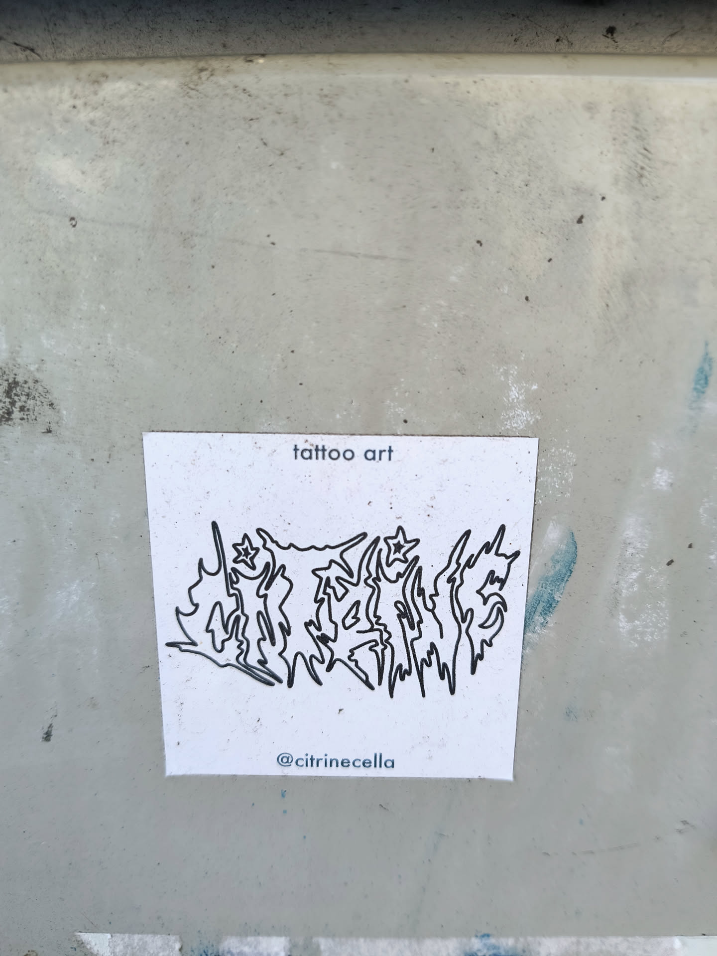 A sticker featuring a black line art design resembling a stylized logo or lettering. The words \"tattoo art\" are written at the top, and the artist's Instagram handle is at the bottom. The style is reminiscent of blackwork tattoos.