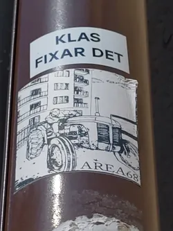 A sticker featuring a black and white drawing of a tractor in front of an apartment building. The text 'KLAS FIXAR DET' is visible at the top, and 'AREA68' is at the bottom.