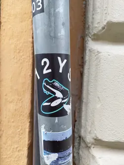 A sticker featuring a black and white illustration of a soccer cleat placed on a vinyl record. The sticker has a black background with white and light blue accents.  The text "12YS" is partially visible on the sticker.