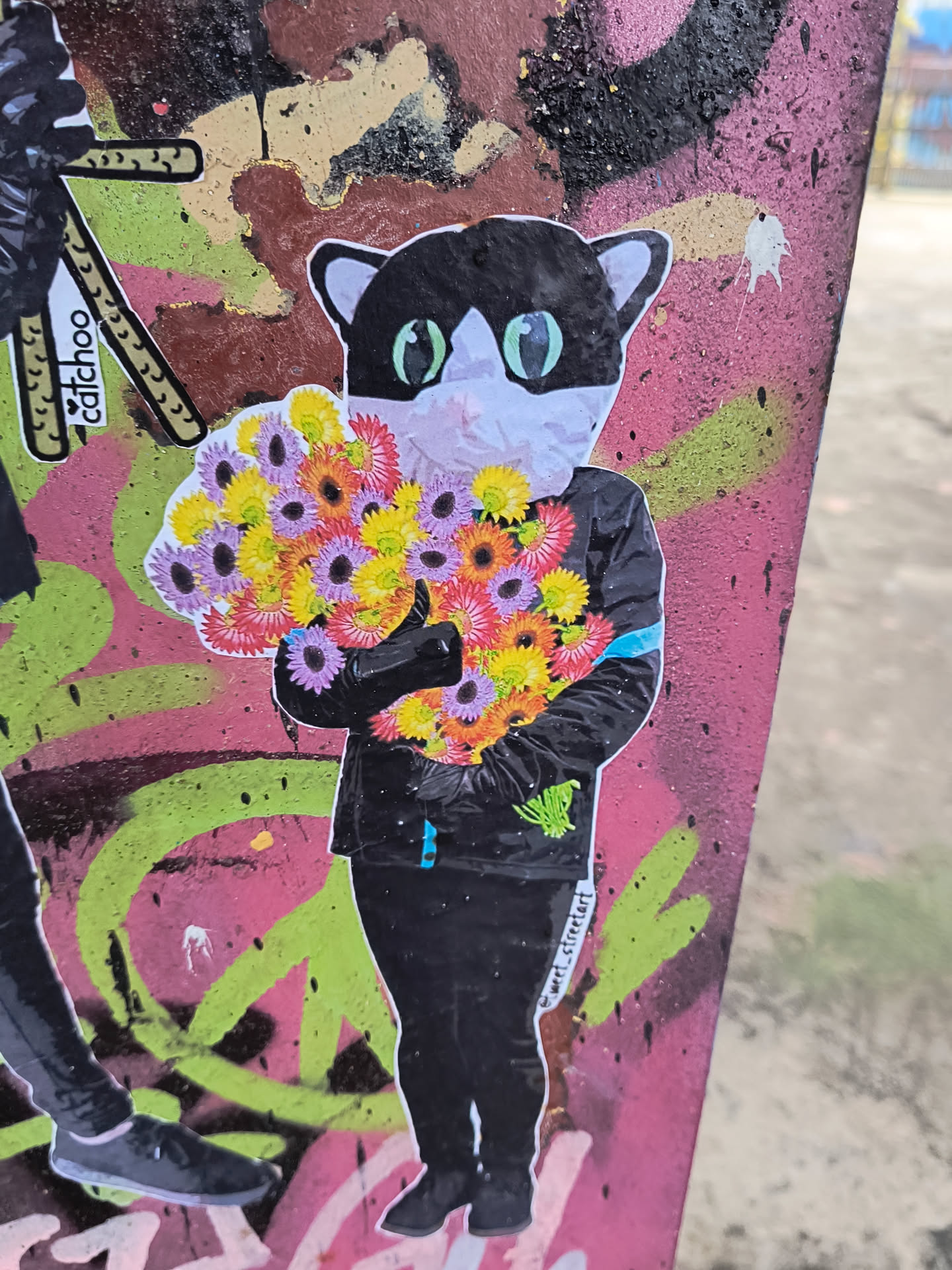A cat wearing a black jacket holds a bouquet of flowers. The sticker has a collage-style aesthetic with a mix of colorful elements.