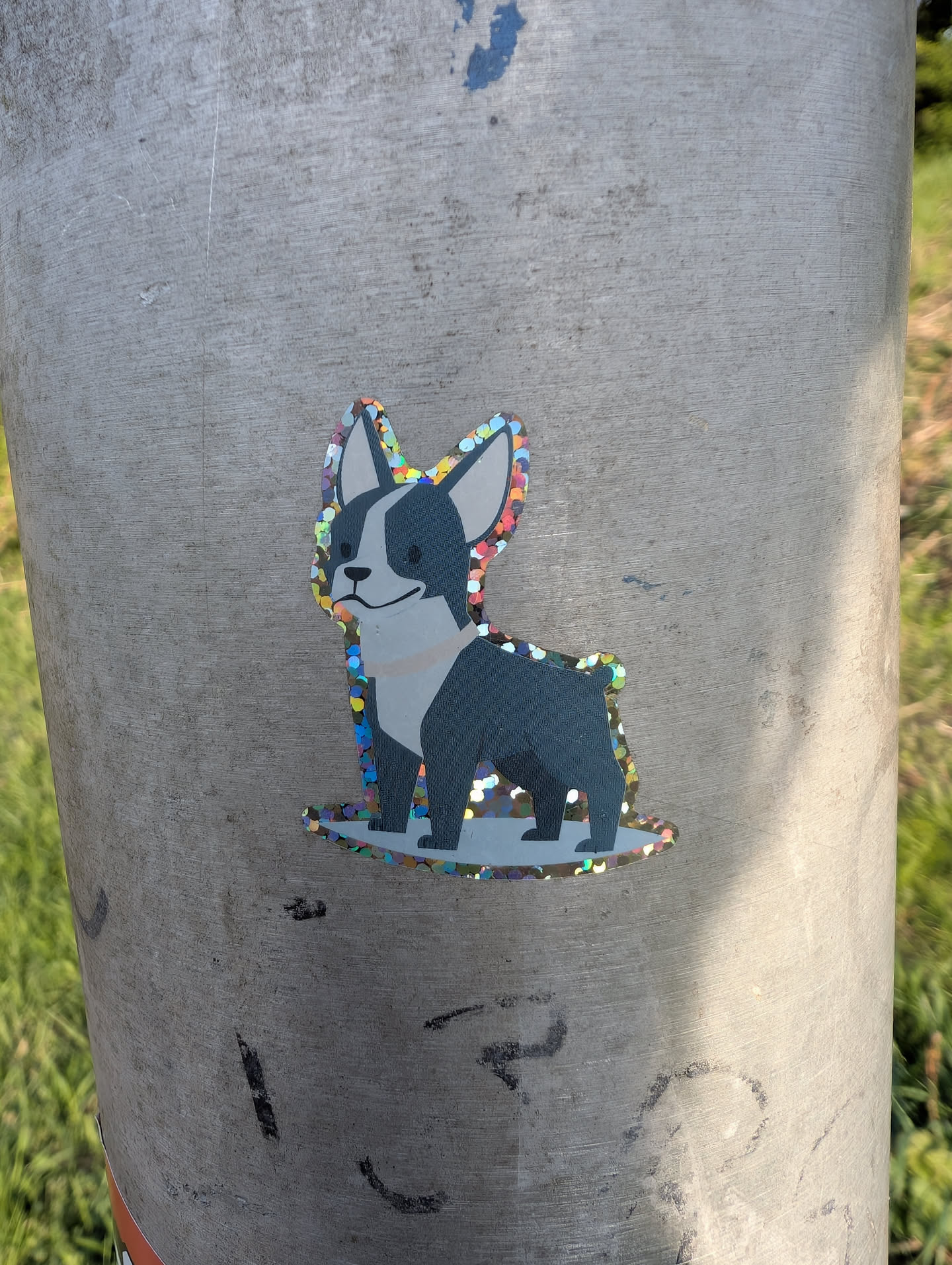 A sticker of a Boston Terrier dog, the sticker has a glittery finish. The dog has black and white markings and is standing on a glittery base.