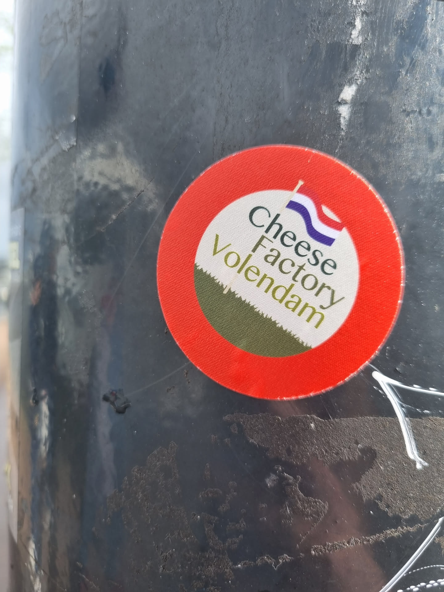 A round sticker with a red border and a white center.  The text 'Cheese Factory Volendam' is written on it, along with a small image of the Dutch flag.