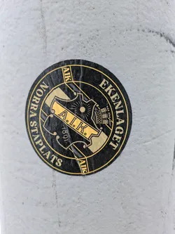 Black and gold round sticker with the text "AIK Ekenlaget Norra Stapla plats" and the year 1891.  The sticker features a crest-like emblem.