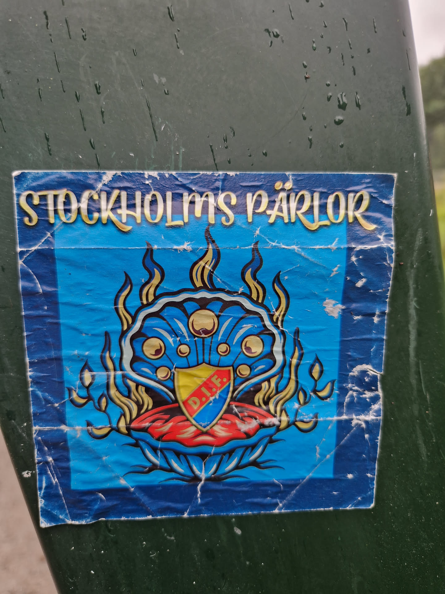 A sticker featuring a blue and gold design with a clam shell and flames. It says "Stockholms Pärlor" at the top. There is a shield inside the clam with the letters D.I.E.