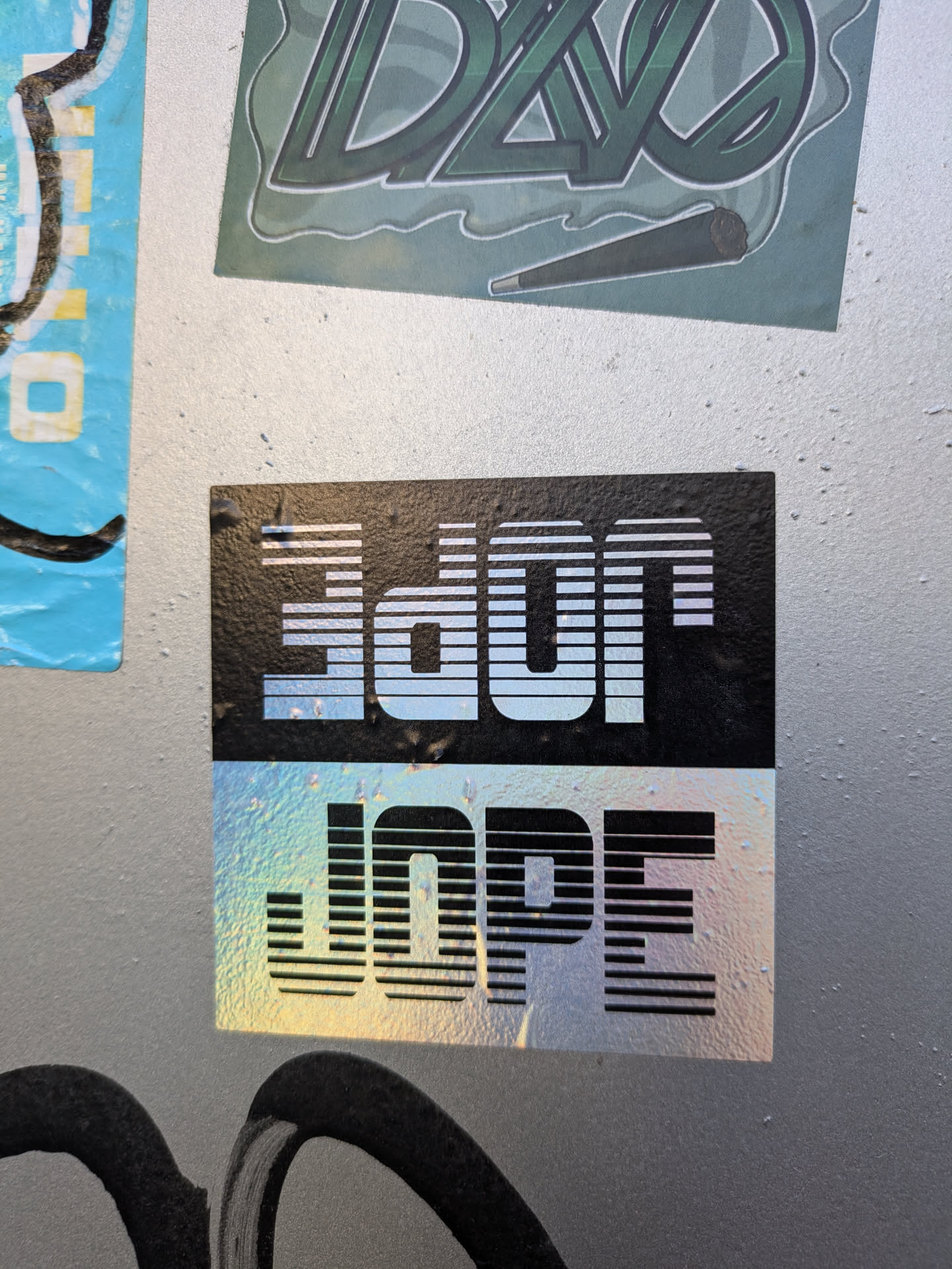 A holographic sticker with the word "DOPE" stacked on top of "JOPE" in a retro style font. The sticker has a black background and a iridescent effect.