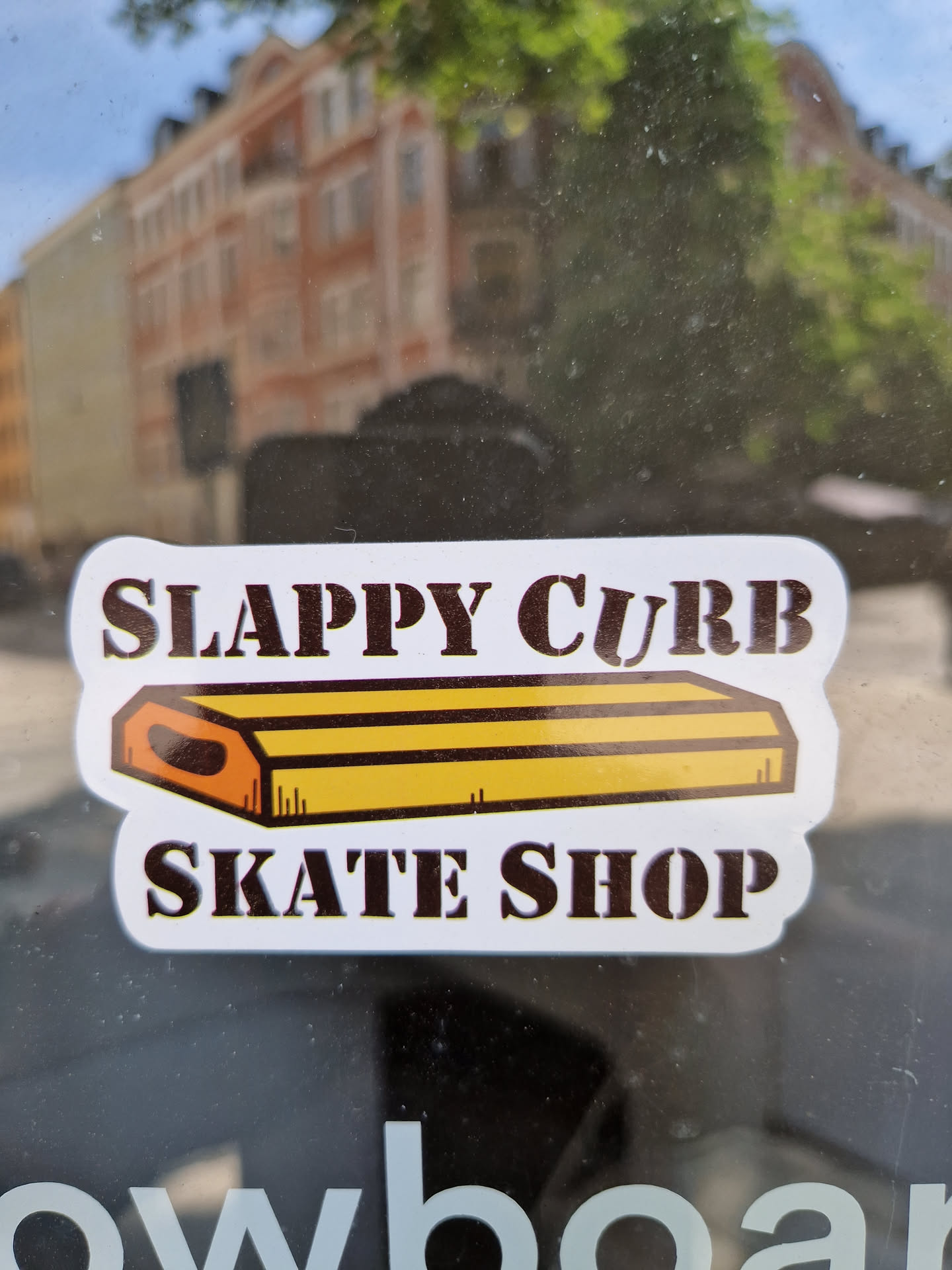 A sticker featuring a cartoon illustration of a skate curb and the text 'Slappy Curb Skate Shop'. The sticker is white with brown and yellow illustrations and text.
