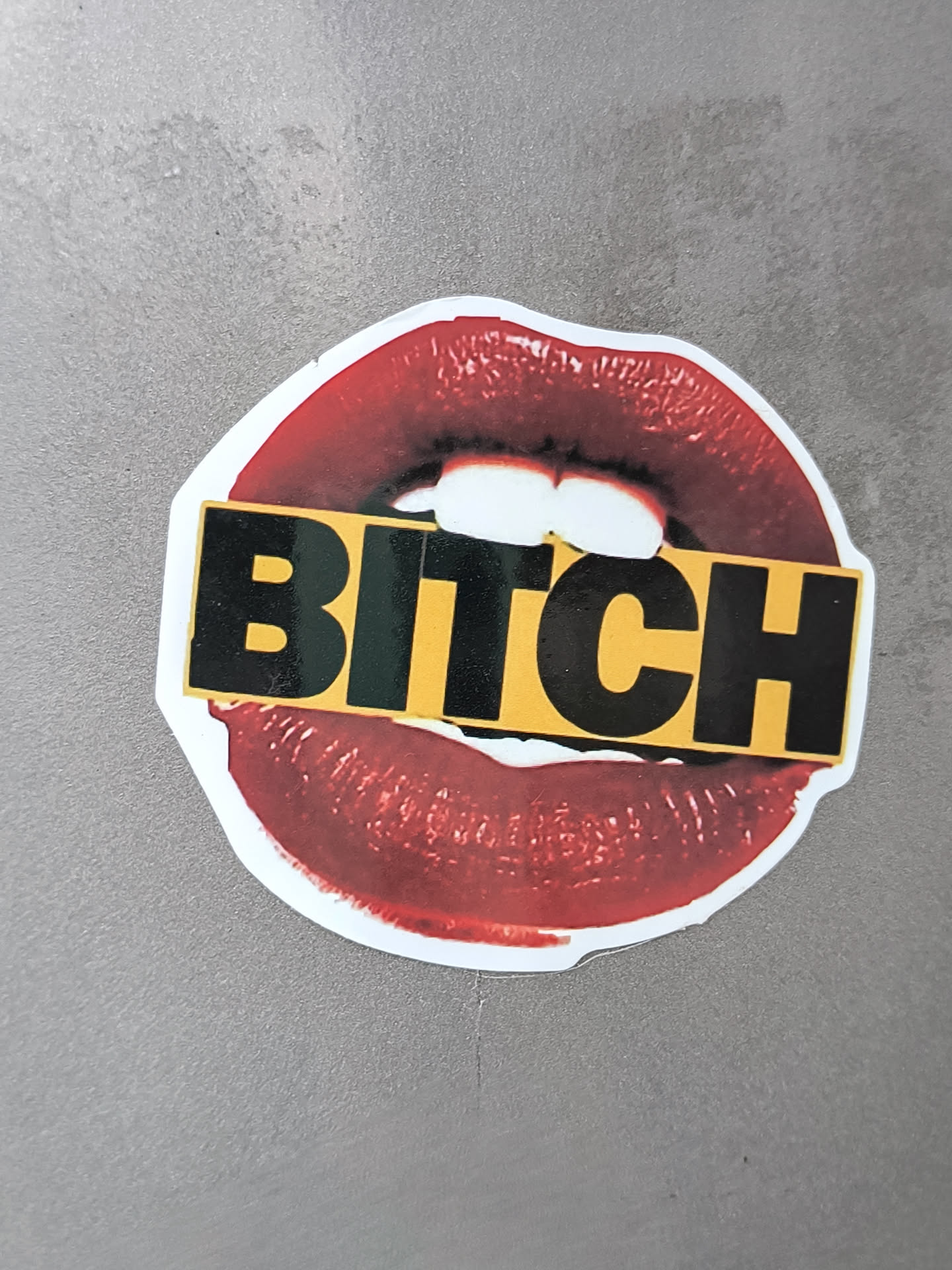 A sticker of a pair of red lips with the word BITCH in bold black letters on a yellow background across the lips.