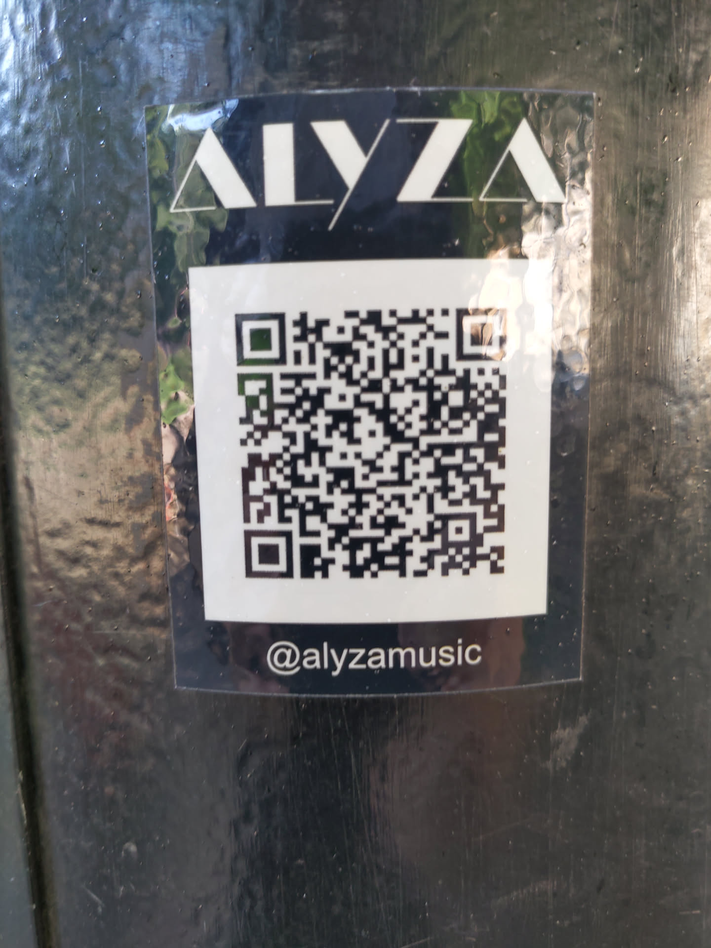 Black and white sticker with the artist's name Alyza in a stylized font, a QR code, and the social media handle @alyzamusic. 