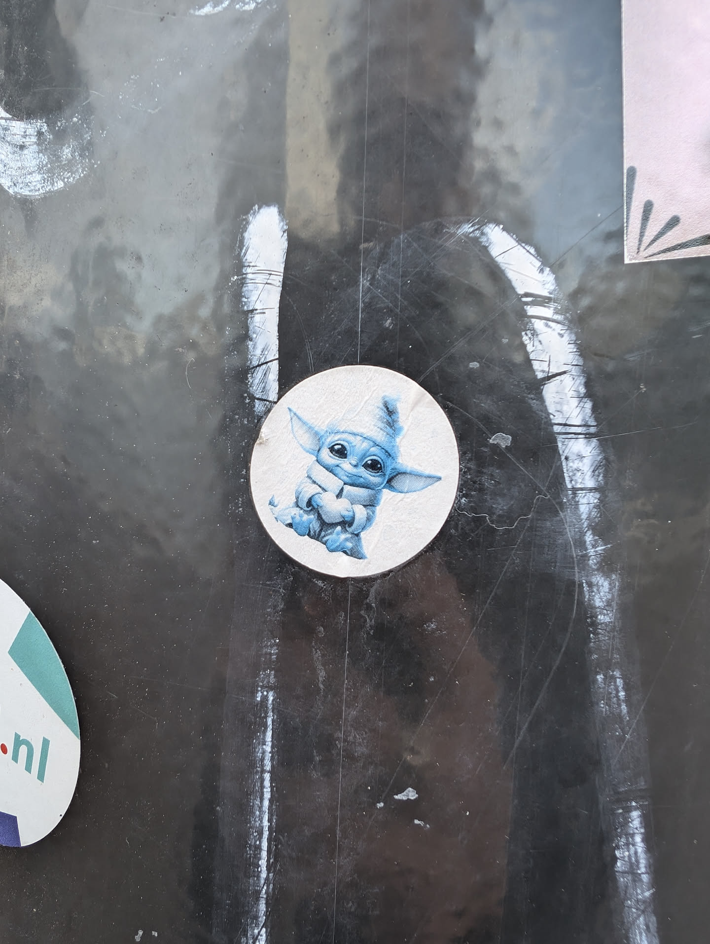 A small, round sticker featuring a cute illustration of Grogu (aka Baby Yoda) from the Mandalorian series.  The sticker is light-colored with a blue Grogu sitting down.