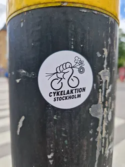 A sticker featuring a fist holding flowers above a bicycle. The text below says "Cykelaktion Stockholm".