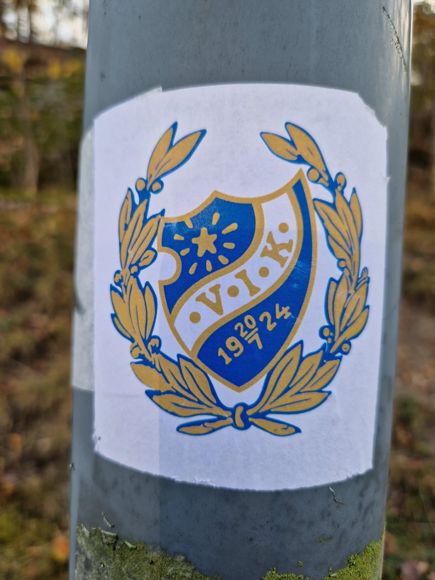 A sticker featuring a blue and gold crest with the letters V.I.K. and the years 1920 and 1924. The crest is surrounded by a laurel wreath.  It's likely related to a sports club or organization.