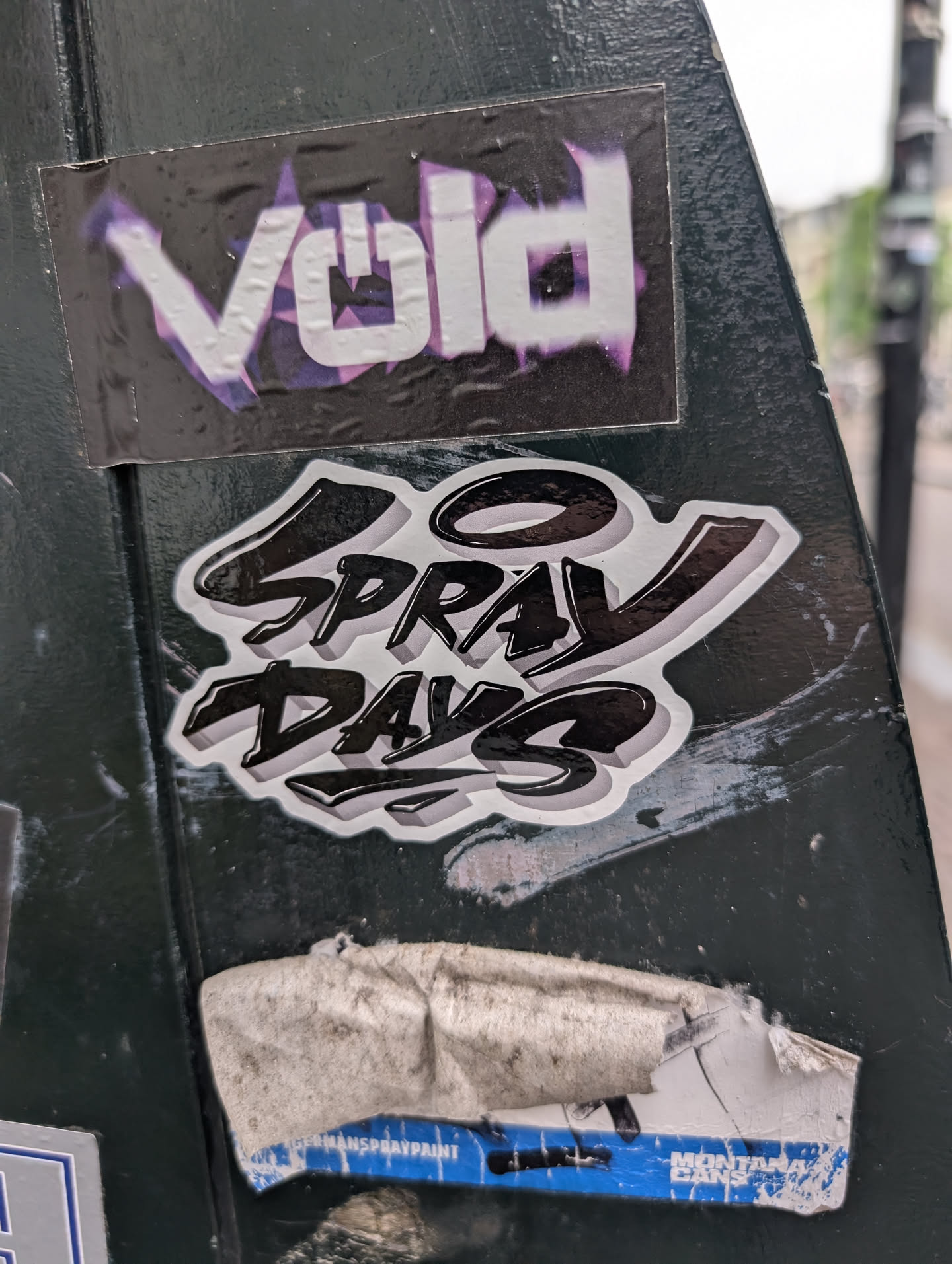 The sticker says "50 Spray Days" in a stylized font. The sticker is black and white with a 3D effect. The background is a dark green surface.