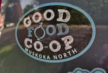 Oval sticker with the text "GOOD FOOD CO-OP" in a stylized font. Below the main text is "MUSKOKA NORTH". A drawing of an onion is between the words "FOOD" and "CO-OP". The sticker has a dark background with light blue text and accents.