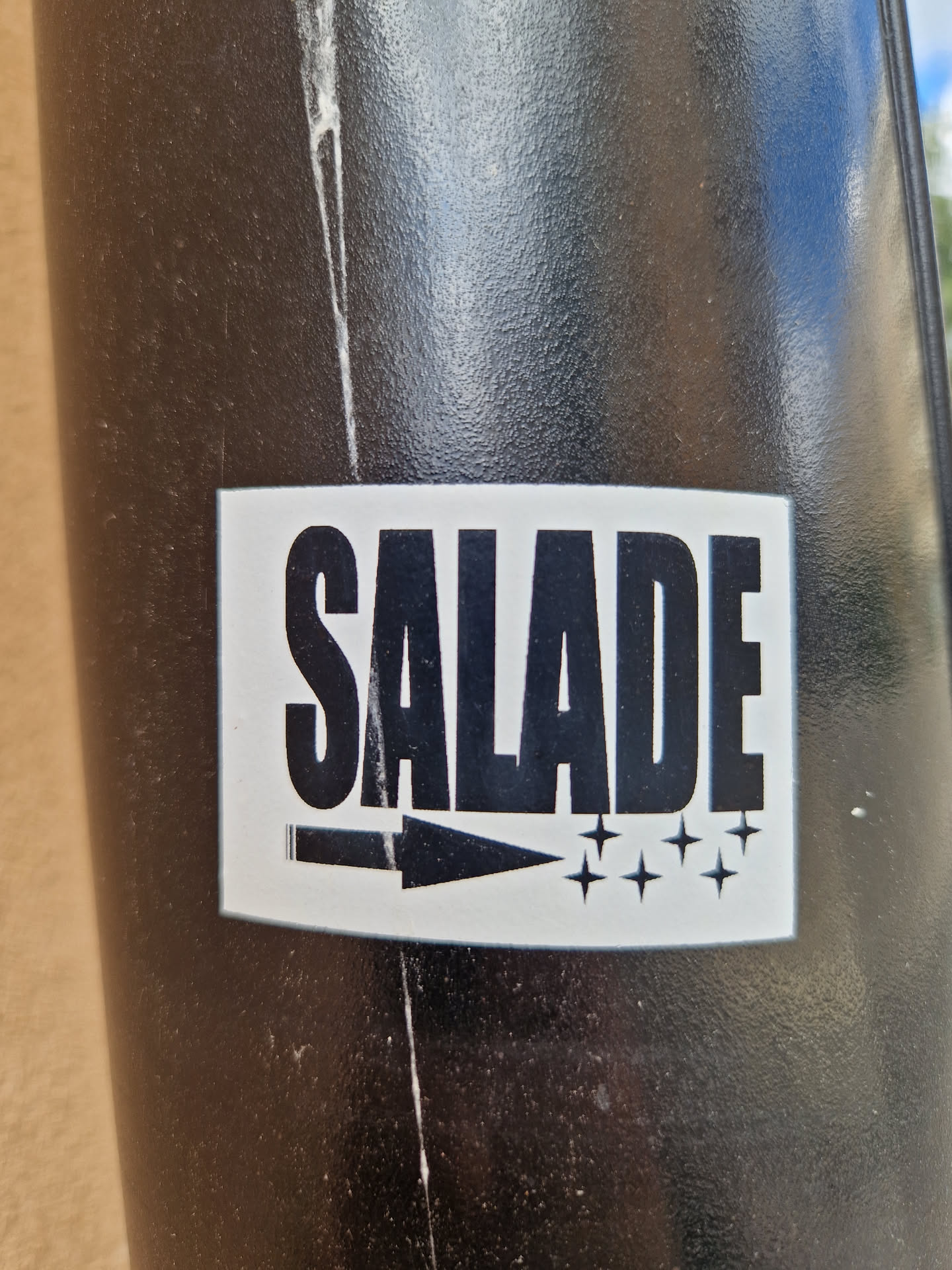 A black and white sticker with the word SALADE (French for salad) in bold capital letters. It features an arrow pointing to the right and several small stars.