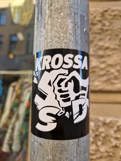 Black and white sticker with the word KROSSA and an illustration of a hand. The style is reminiscent of street art or graffiti.