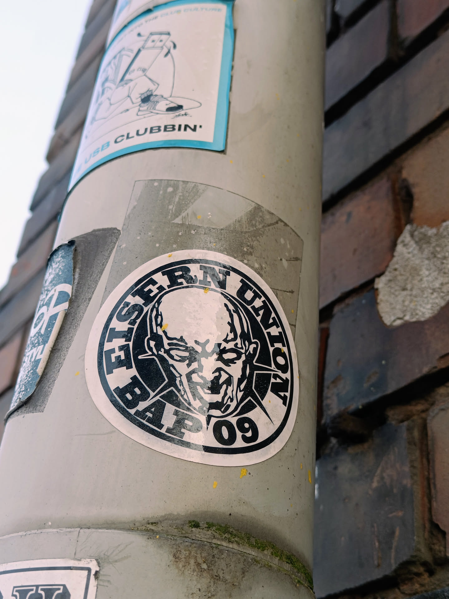 A black and white sticker with a skull-like figure in the center. The text around it says "Eiserne Union Bap 09".