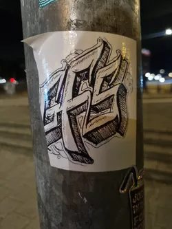 This sticker showcases a unique blend of artistic styles. The central motif is a graphic representation of stylized lettering, possibly an abbreviation or logo. The design is rendered in a bold, almost three-dimensional manner, with heavy use of shading and line work to create a sense of depth and texture. The overall aesthetic suggests a street art or graffiti influence.