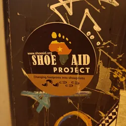 A round sticker with the Shoe Aid Project logo.  The logo features a footprint in the shape of the African continent with a yellow star, and the text 'Shoe Aid Project'.  The sticker also includes the website address www.shoeaid.org and the tagline 'Changing footprints into shoeprints'.