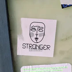A sticker with a minimalist line art face and the word STRONGER written underneath. The style is simple and modern, conveying a message of empowerment.