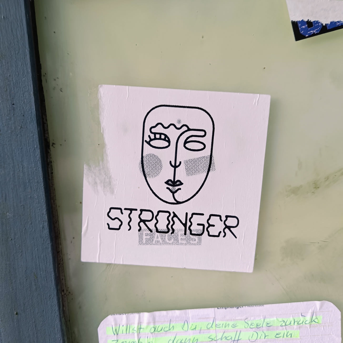 A sticker with a minimalist line art face and the word STRONGER written underneath. The style is simple and modern, conveying a message of empowerment.