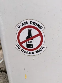 This is a sticker that features a bottle, with the size 0.33 on it, inside a red circle with a line through it, indicating "no alcohol". Above and below the circle is the text "V-AM PRINS CU OCAUA MICA."